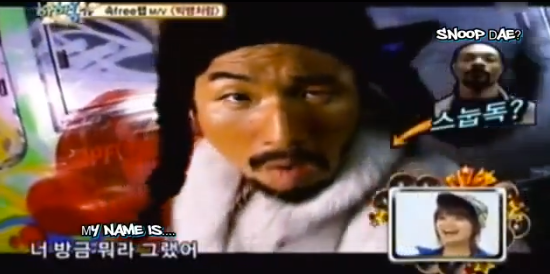 Daesung with braids and dark face makeup in a big white jacket imitating snoop dogg